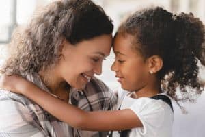 African-american mother and small little young preteen daughter hugging embracing with eyes closed sharing love and care.