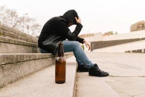 Close-up of a beer bottle on the floor with a drunk young man crying having problems