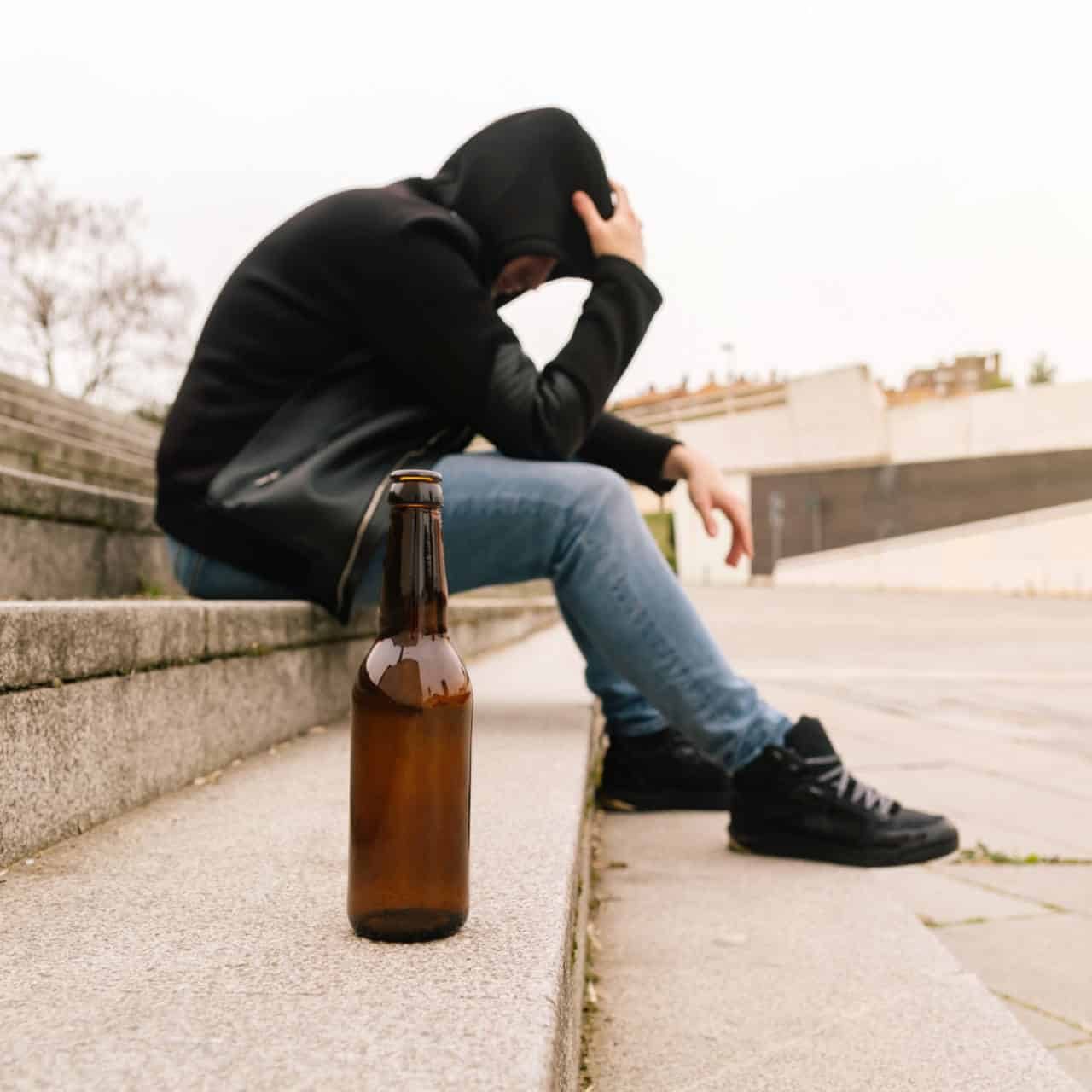Close-up of a beer bottle on the floor with a drunk young man crying having problems.